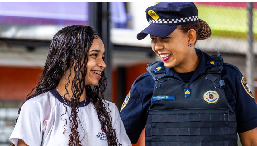 foto de uma estudante e uma guarda municipal, ambas se entreolham sorrindo