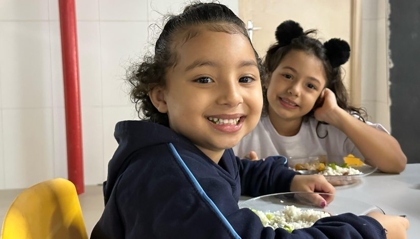 Duas crianças com pratos de comida sorriem para a foto
