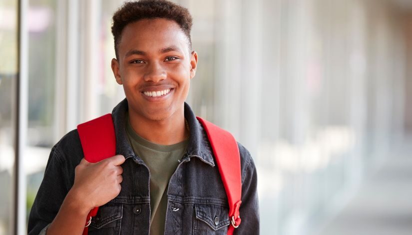 Foto de um estudante negro, com uma mochila vermelha em suas costas.