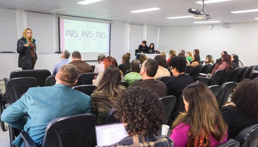 Fotografia dos Seminários Juntos Pela Aprendizagem mostra uma mulher em pé falando para várias pessoas sentadas no auditório.