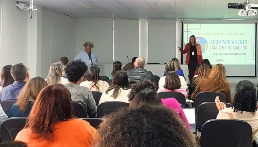 Fotografia mostra profissionais da Educação reunidos no auditório para os