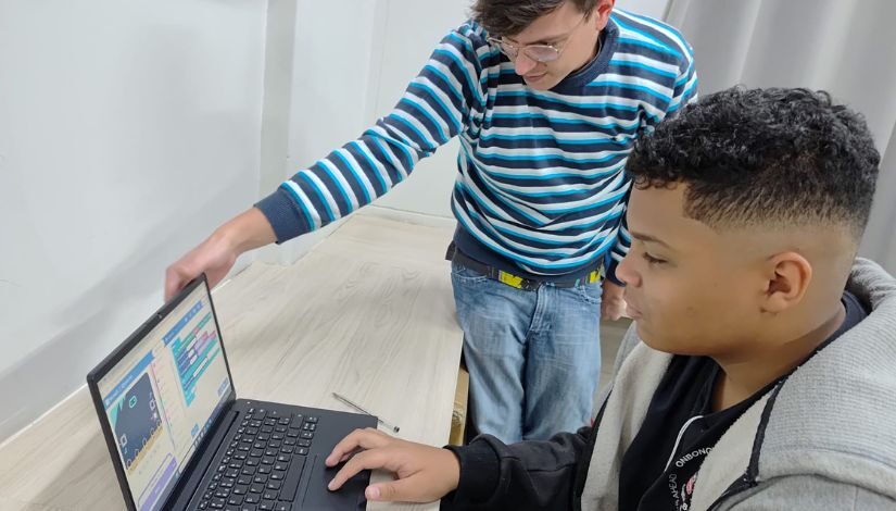 Fotografia de um estudante e professor com o computador portátil sobre a mesa aprendendo programação em atividade relacionada a COP30.