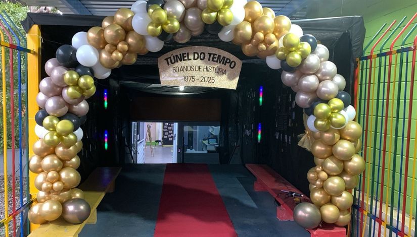 Fotografia de um túnel do tempo que começa com arco de balões dourados, brancos e pretos da história da EMEI Machado Assis em seus 50 anos.