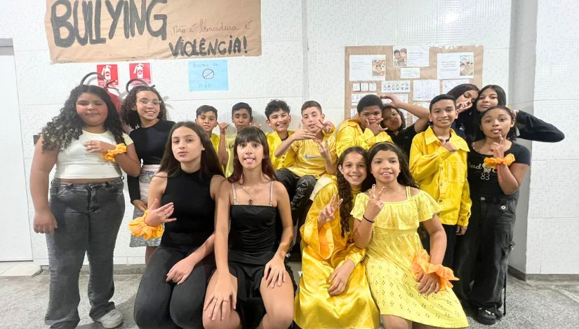 Fotografia de estudantes da EMEF Antonia e Artur Begbie, alguns vestidos com roupas pretas outros com amarelas para apresentação de teatro.