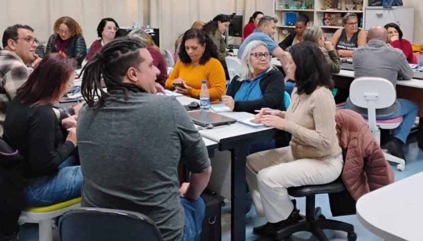 Fotografia mostra educadores reunidos em volta das mesas