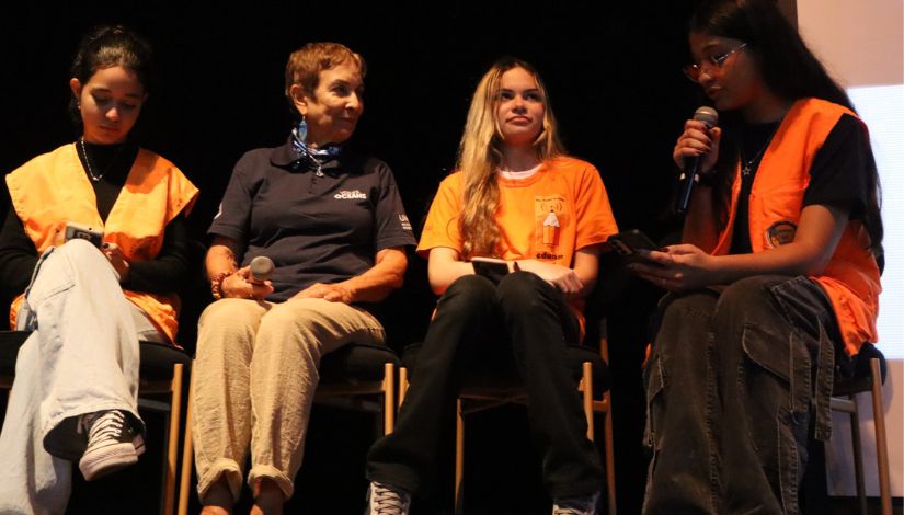 Fotografia de 4 mulheres sentadas em cadeiras. Três delas são estudantes do Programa Imprensa Jovem que entrevistam a escritora Heloisa Schurmann.