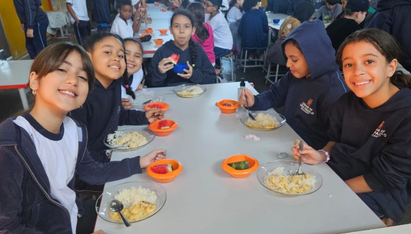 Estudantes sentados ao redor da mesa se alimentando