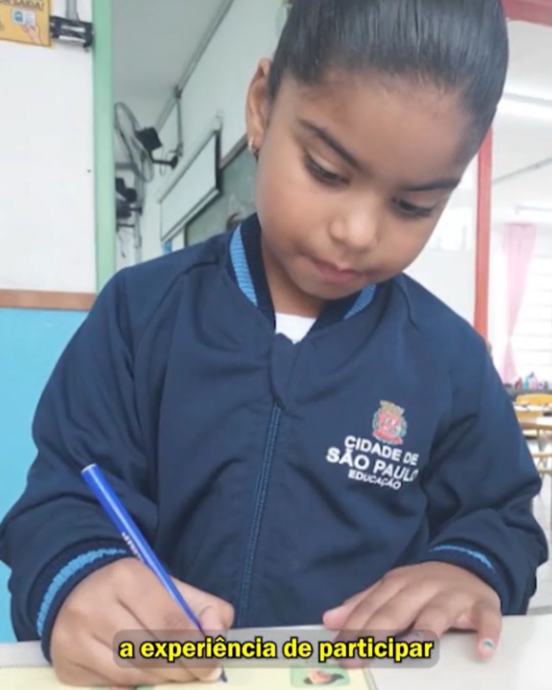 Estudante com casaco azul e caneta na mão assinando papel.
