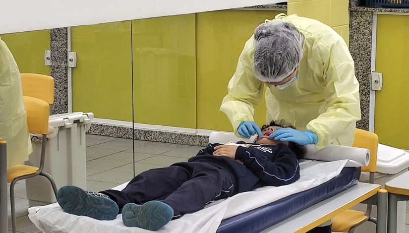 Fotografia de um estudantes deitado sobre uma mesa com colchonete, recebendo atendimento odontológico em uma ação do Dia B.