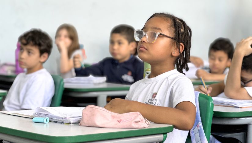 Fotografia de sala de aula com estudantes sentados em suas carteiras.