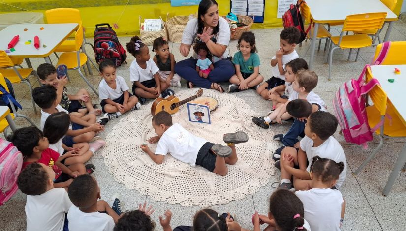 Roda de conversa de crianças pequenas sentadas no chão com a professora para leitura de uma história.