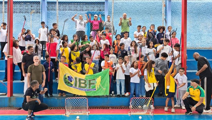 Grupo de estudantes segurando tacos e uma bandeira escrito IBF. Eles estão acompanhados de adultos.