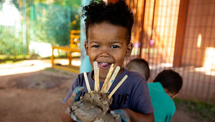 Criança com um bolo de argila na mão cheio de palitos de sorvete no topo.