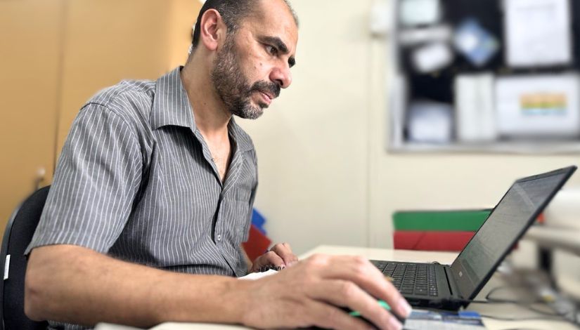 Fotografia de um homem sentado a frente do seu computador de mesa.