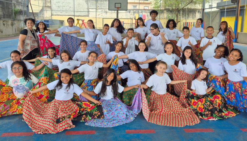 Fotografia de uma turma de meninas com suas saias rodadas de chita colorida na quadra da escola.