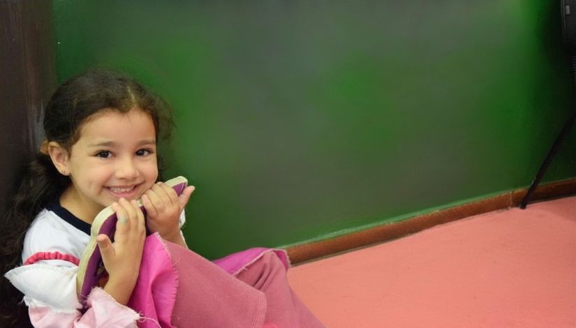 Fotografia de uma menina sentada no chão abraçando um livro e sorrindo.
