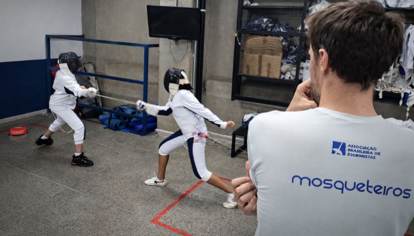 Dois estudantes treinando esgrima e o professor observando.