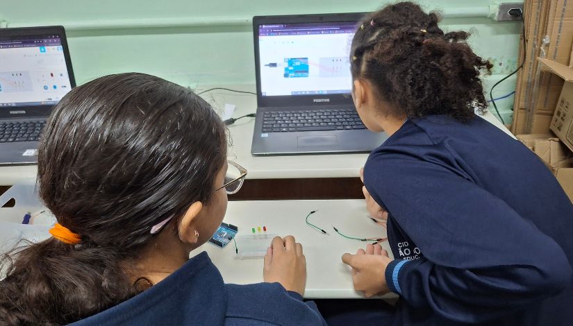 Fotografia de duas meninas de costas para a câmera fotográfica e olhando para a tela de um computador.