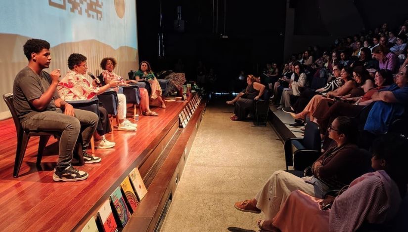 Fotografia de pessoas em um palco com a platéia repleta de pessoas.