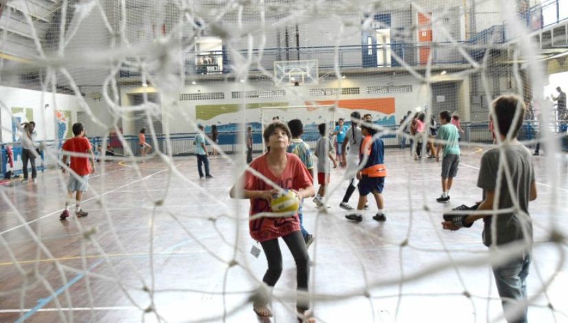 Fotografia de meninos na quadra jogando futsal. Em primeiro plano o fundo da rede.