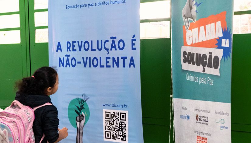Fotografia de uma menina olhando para um cartaz com as frases 