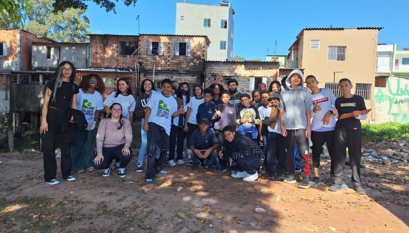 Grupo de estudantes e educadoras reunido em atividade de campo próxima ao Córrego Jacupeval. Os participantes posam para foto em área urbana, durante ação de educação ambiental e estudo do território.