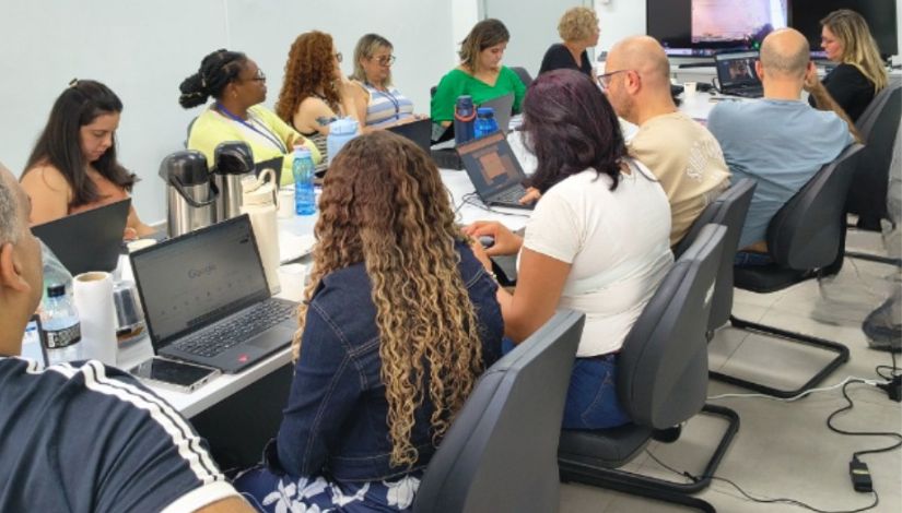 Fotografia de adultos sentados ao redor de uma mesa com computadores portáteis.