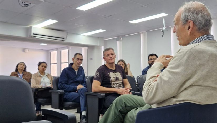 Fotografia do professor José Moran sentado conversando com pessoas em um auditório.