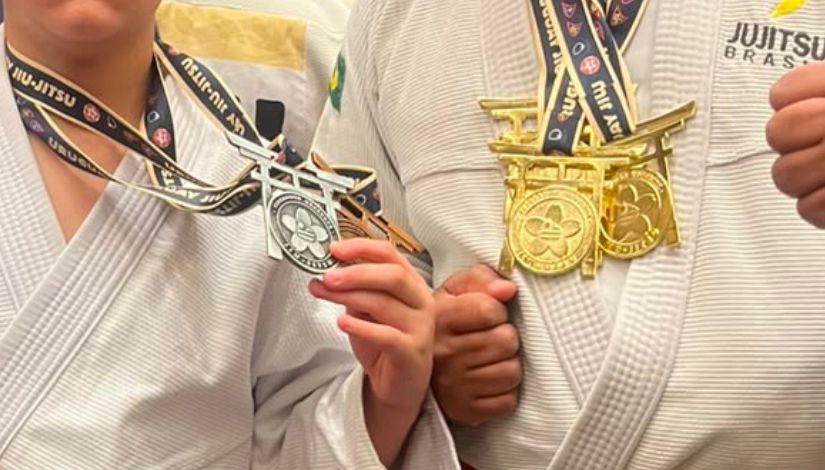 Fotografia de melhadalhas de ouro, prata e bronze no pescoço de dois atletas coom uniforme de ju-jitso.