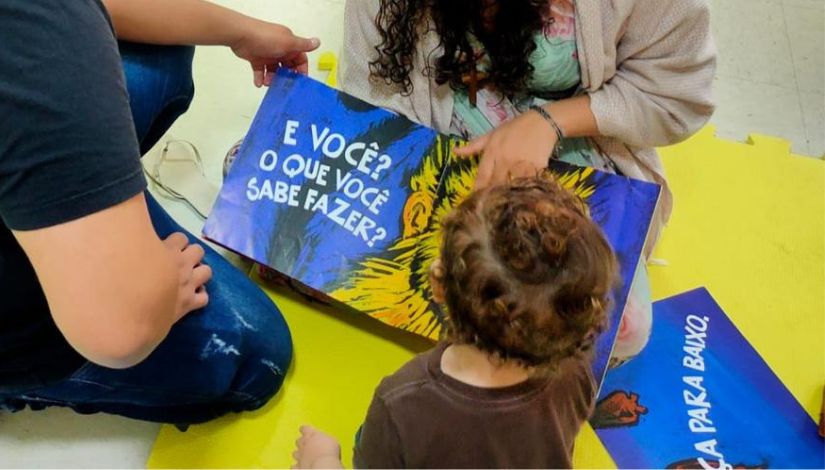 Fotografia de um bebê de costas olhando as páginas de um livro.