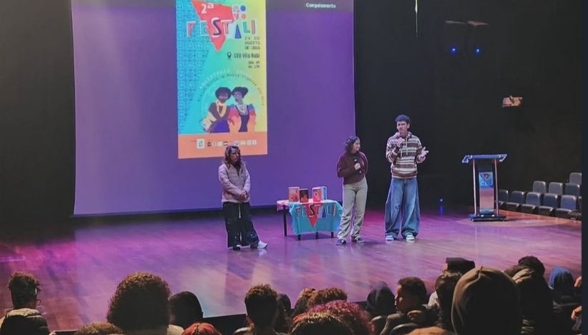 Fotografia de três jovenes ao palco. Ao fundo, uma projeção com o logotipo da 2ª Edicação da Festali.