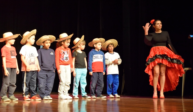sete crianças com chapéu de palha ao lado de uma mulher vestida de preto e vermelho como roupa flamenca
